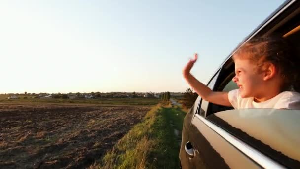 Niña mirando por la ventana del coche y agitando su mano — Vídeos de Stock