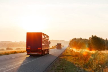 Gün batımında kırsal bir arazide yola çıkan bir kamyon.