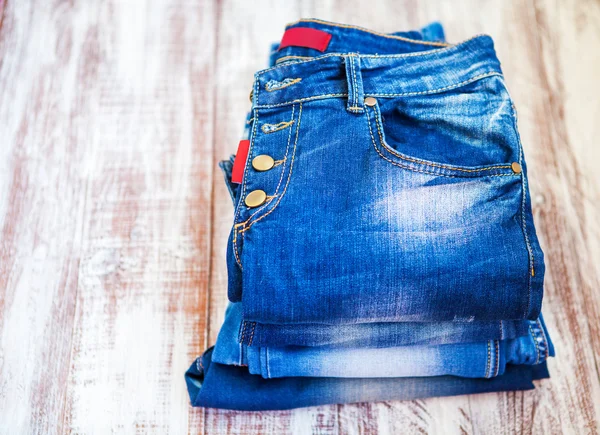 Jeans stacked on a wooden background — Stock Photo, Image