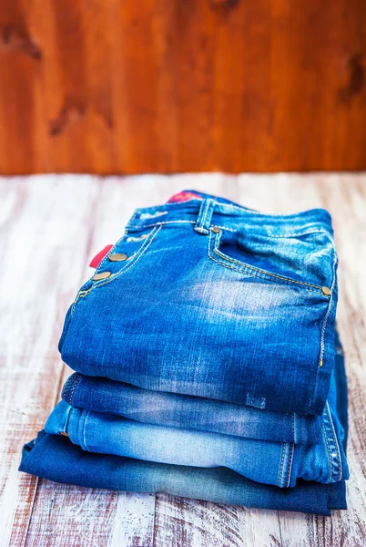Jeans stacked on a wooden background — Stock Photo, Image