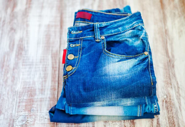 Jeans stacked on a wooden background — Stock Photo, Image