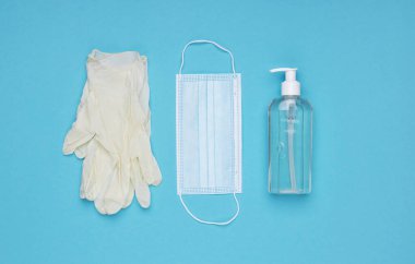 Yüz maskesi, el dezenfektanı şişesi ve lateks eldivenler. Coronavirus önleme tıbbi maske, el dezenfektanı jeli, el hijyen koronavirüsü koruması. Mavi bir arkaplanda.