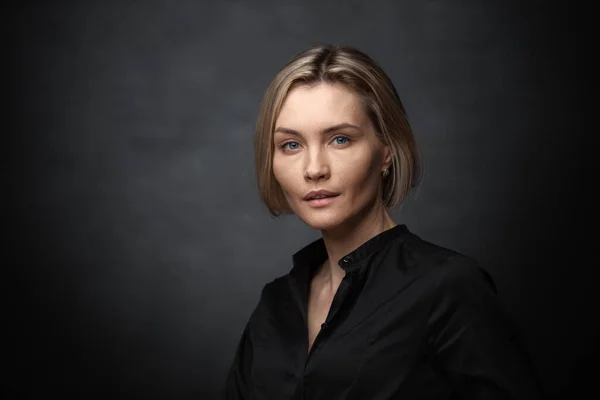 Mooie middelbare leeftijd vrouw op een grijze achtergrond in een zwarte blouse. — Stockfoto