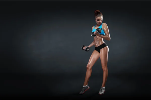 Fitness girl with dumbbells on a dark background — Stock Photo, Image