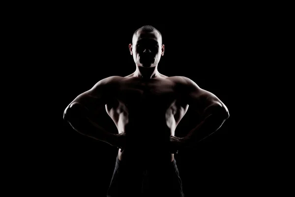 Kulturista ukazuje bicepsy na tmavém pozadí — Stock fotografie