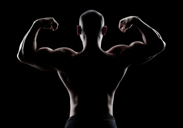 Bodybuilder visar biceps bakifrån på en mörk bakgrund — Stockfoto