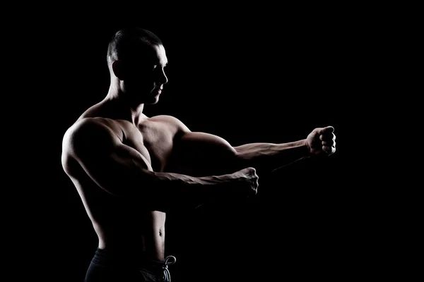 Bodybuilder demonstrates biceps on a dark background — Stock Photo, Image