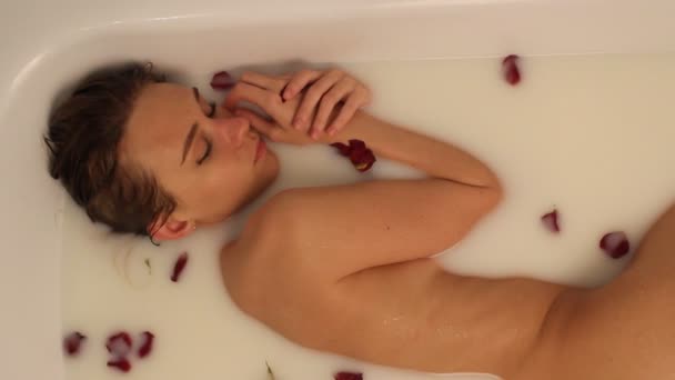 Muchacha atractiva en baño con leche y pétalos de rosa. Tratamientos spa para el rejuvenecimiento de la piel. Mujer atractiva con maquillaje brillante en el salón de Spa. Bastante sexy morena relajante en jacuzzi con pétalos de flores rojas . — Vídeo de stock