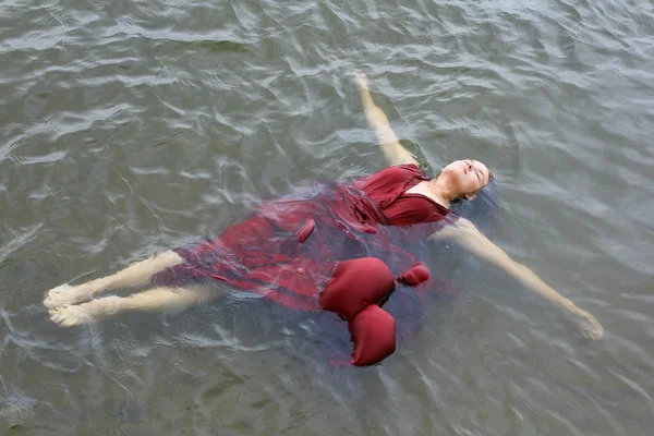 Jeune belle femme noyée en robe rouge couchée dans l'eau en plein air — Photo