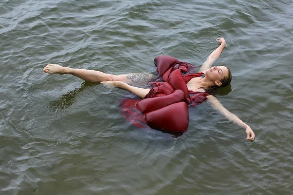 Jonge mooie verdronken vrouw in rode jurk liggend in het water buiten — Stockfoto