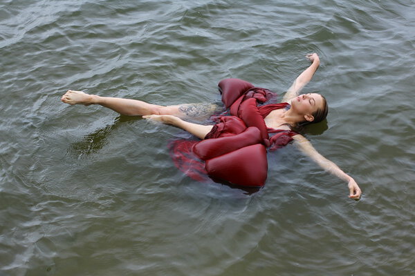 Young beautiful drowned woman in red dress lying in the water outdoor
