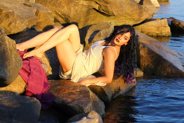 Schöne junge Frau sitzt auf einem Stein am Ufer des Meeres — Stockfoto