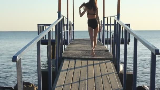 Model in zwarte bikini catwalks landingsbaan op de pier van de zee bij zonsondergang. — Stockvideo