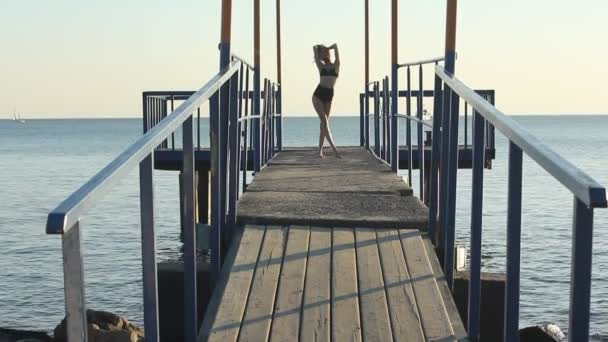 Model w czarnym bikini wybiegach pasa startowego na molo morze o zachodzie słońca. — Wideo stockowe
