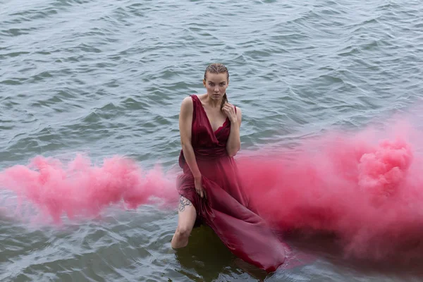 Retrato abstrato. Mulher bonita caminha ao lado do mar. Vestido molhado e vermelho. Nuvem rosa sobre a cabeça. Cores vintage . — Fotografia de Stock