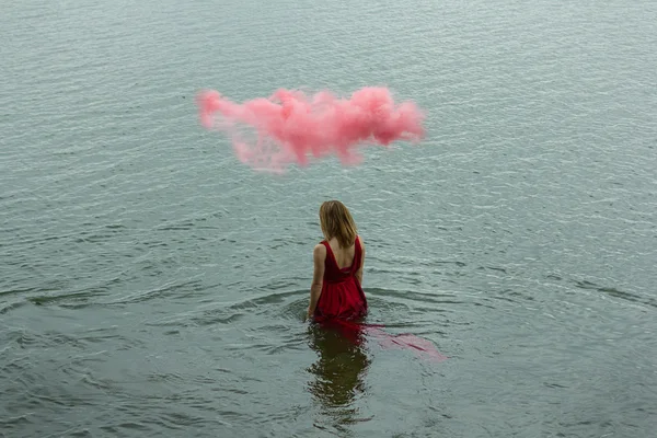 Portrait abstrait. Belle femme marche au bord de la mer. Robe rouge mouillée. Nuage rose sur la tête. Couleurs vintage . — Photo