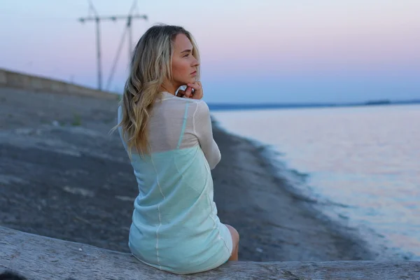 Retrato de jovem mulher encantadora em vestido azul relaxante enquanto sentado perto do oceano na noite de verão, fêmea despreocupada atraente durante o tempo de recreação no fim de semana . — Fotografia de Stock