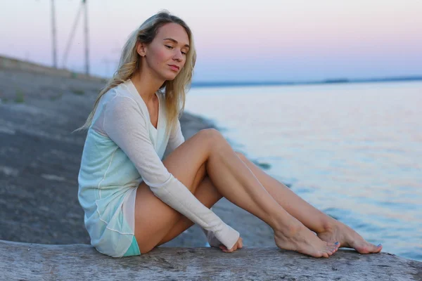 Portrait de jeune femme charmante en robe bleue se détendre tout en étant assis près de l'océan en soirée d'été, belle femme insouciante pendant les loisirs le week-end . — Photo