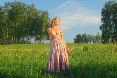 Sexy blond european girl relax in green summer meadow. Sunset in summer nature.