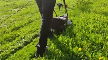 ALTAI KRAI, RUSSIA - 30 Mayıs 2021: İnsanlar evin arka bahçesinde çim biçme makinesi ve benzin makası ile çim biçiyor.