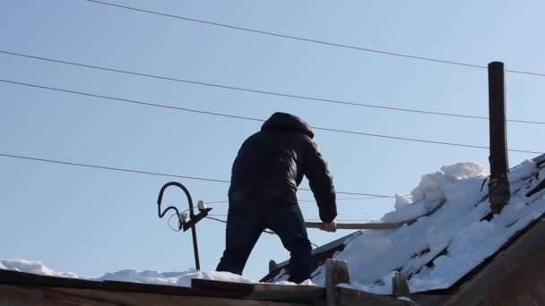 Man verwijderen sneeuw van een dak met een sneeuw shovel — Stockvideo