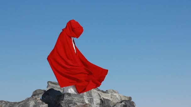 La mariée se tient sur une falaise avec un imperméable rouge fluide sur le vent contre le ciel bleu et le fond d'hiver . — Video