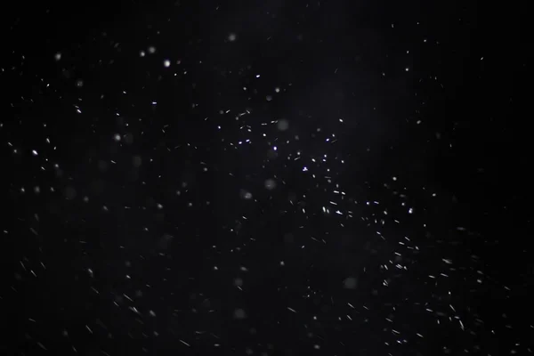 Struttura astratta della tempesta di neve. Bokeh luci su sfondo nero, colpo di volare fiocchi di neve in aria — Foto Stock