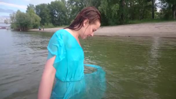 Привлекательная девушка веселится, ныряет и тонет на городском пляже в воде. Женский портрет с синим платьем . — стоковое видео