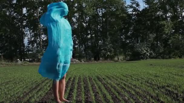 Jonge vrouw met blauwe sjaal wandelingen in de zomer stormachtige veld. — Stockvideo