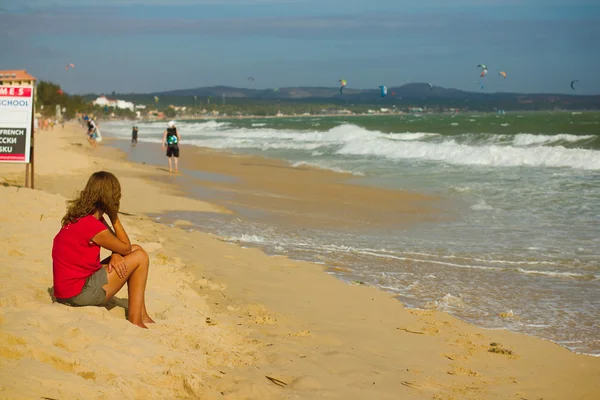 MUI NE, VIETNAM - 25 dicembre 2012: Ragazza sola si siede a riva. Surfisti non identificati che fanno kitesurf al Vietnamita Kiteboard Surf al 25 dicembre 2012 a Mui Ne, Vietnam — Foto Stock