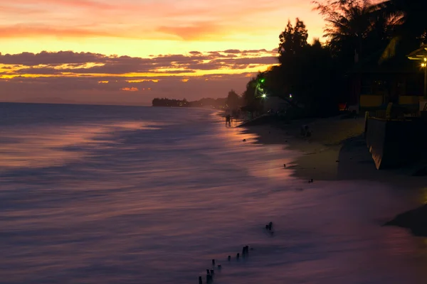 Oceán a písečné pláže, lidí, kteří jdou na západ slunce. — Stock fotografie