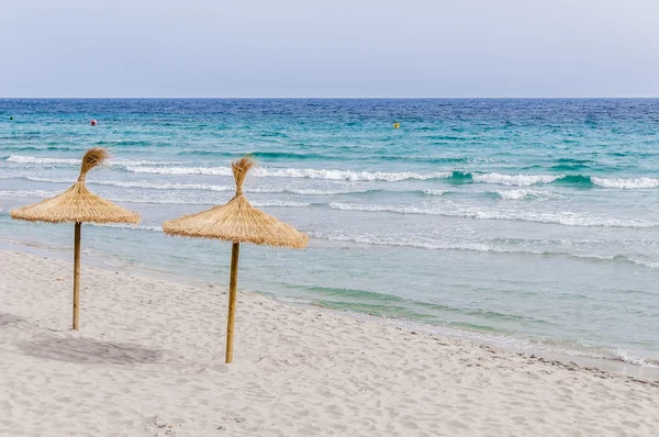 Stro paraplu's op zand strand. — Stockfoto