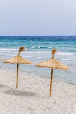 Kum plajı üzerinde hasır şemsiyeler.