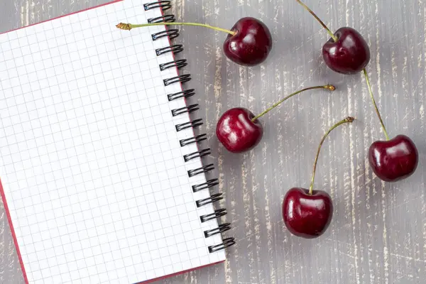 Cerejas frescas e caderno em branco. — Fotografia de Stock