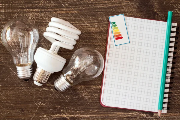 Light bulbs and notebook with energy efficiency label — Stock Photo, Image