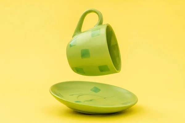 黄色の背景に浮かぶプレートと空の緑のカップ — ストック写真
