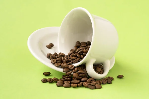 Witte Beker Gevuld Met Gebrande Koffiebonen Vallen Een Groene Achtergrond — Stockfoto