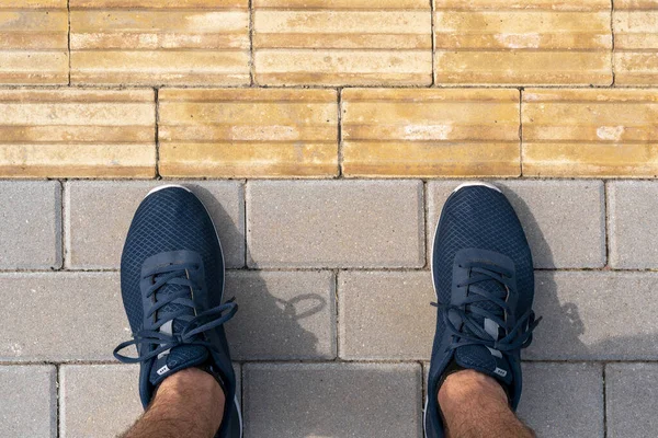 Man standing near the tactile paving for blind handicap. Yellow tactile paving for the visually impaired on the sidewalk.