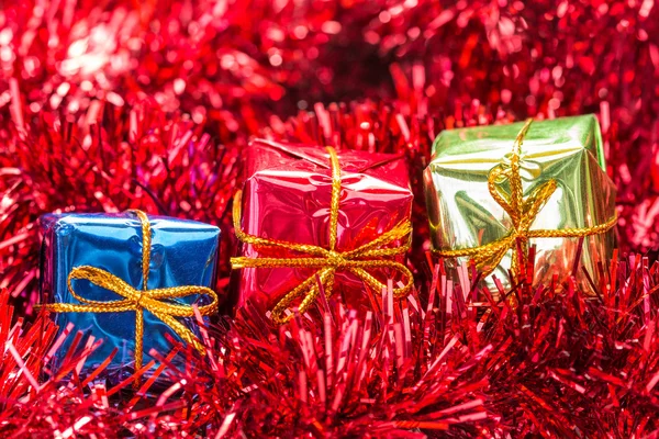 Three gift boxes on red tinsel — Stock Photo, Image