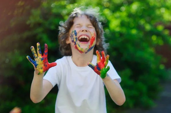 De jongen lacht, zijn gezicht en handen in de verf — Stockfoto