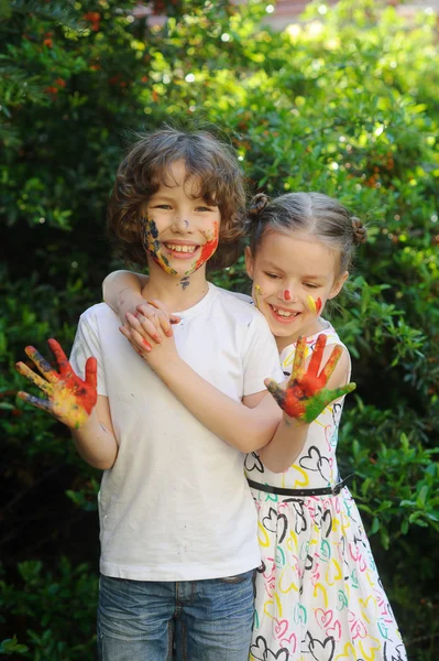 Los niños se abrazan, sus rostros y manos en la pintura — Foto de Stock