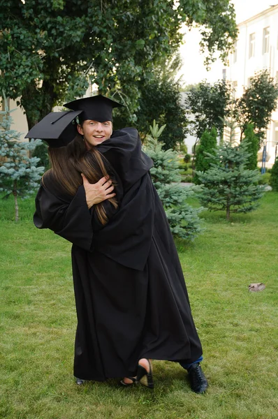 Estudiante en ropa negra se gradúa juguetonamente abraza chica — Foto de Stock