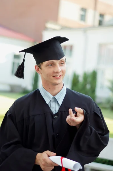 O graduado com um diploma na mão e manto preto — Fotografia de Stock