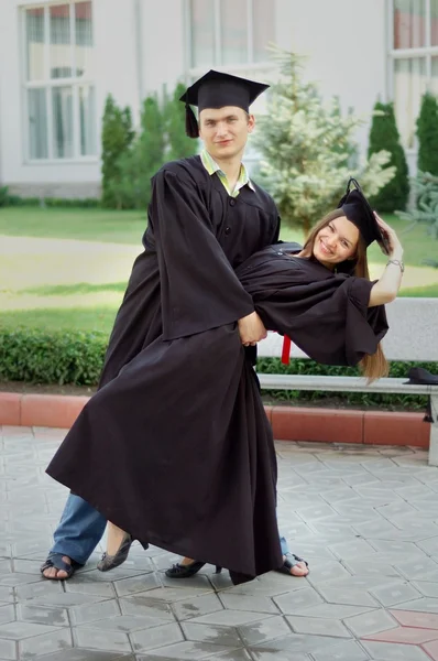 Joven hombre y mujer bailando felizmente en ropa graduados — Foto de Stock