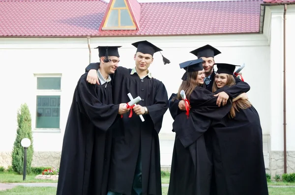Graduados con diplomas en sus manos felizmente se abrazan — Foto de Stock