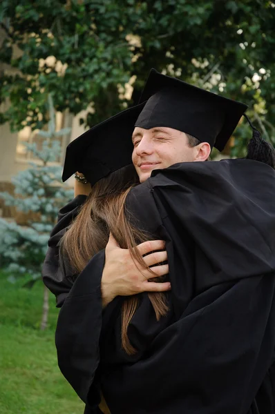 O estudante em um vestido preto graduado abraçando colega de classe . — Fotografia de Stock