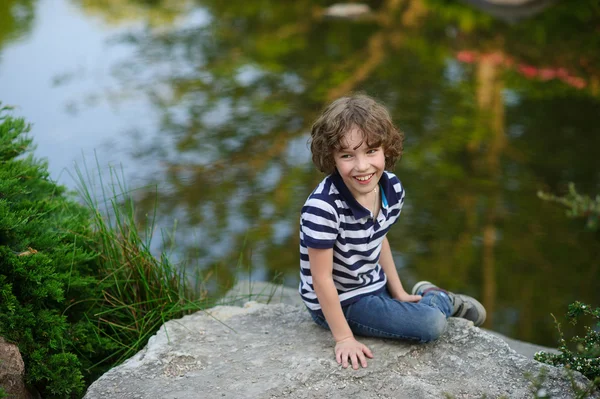 Niño riendo mientras se sienta en la orilla del lago —  Fotos de Stock