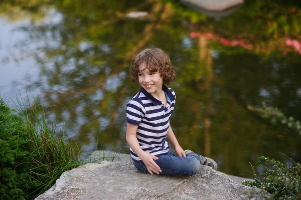 Niño sentado en una roca en el pintoresco estanque — Foto de Stock