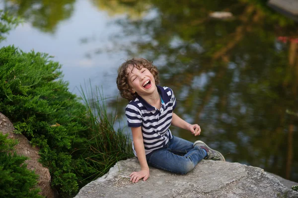 Lachende jongen zittend op het rotsblok in een vijver. — Stockfoto