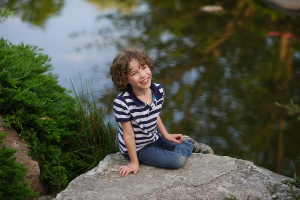 微笑的男孩坐在池塘边 — 图库照片